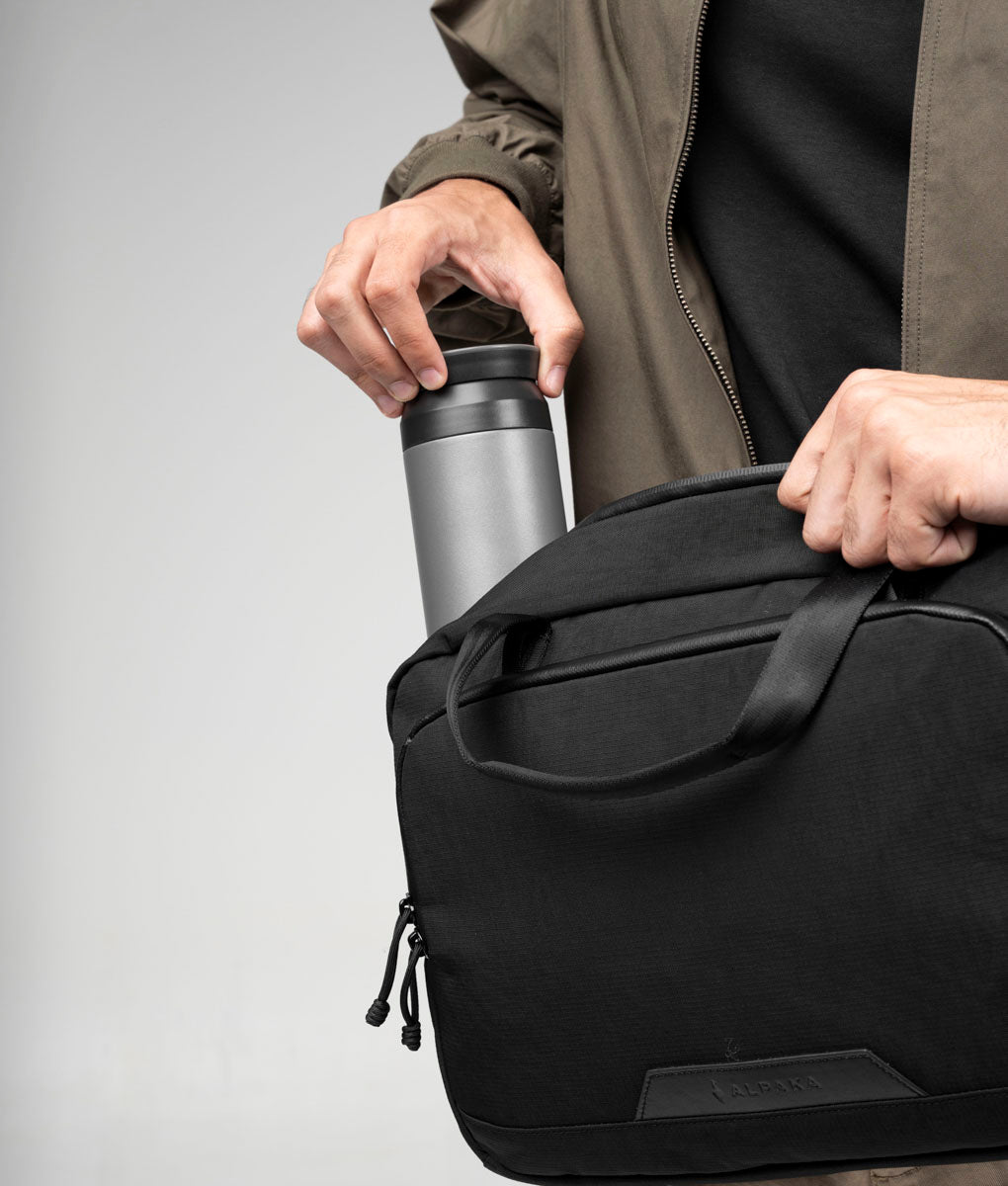A bottle being placed into the main compartment of the black Bravo Brief 14