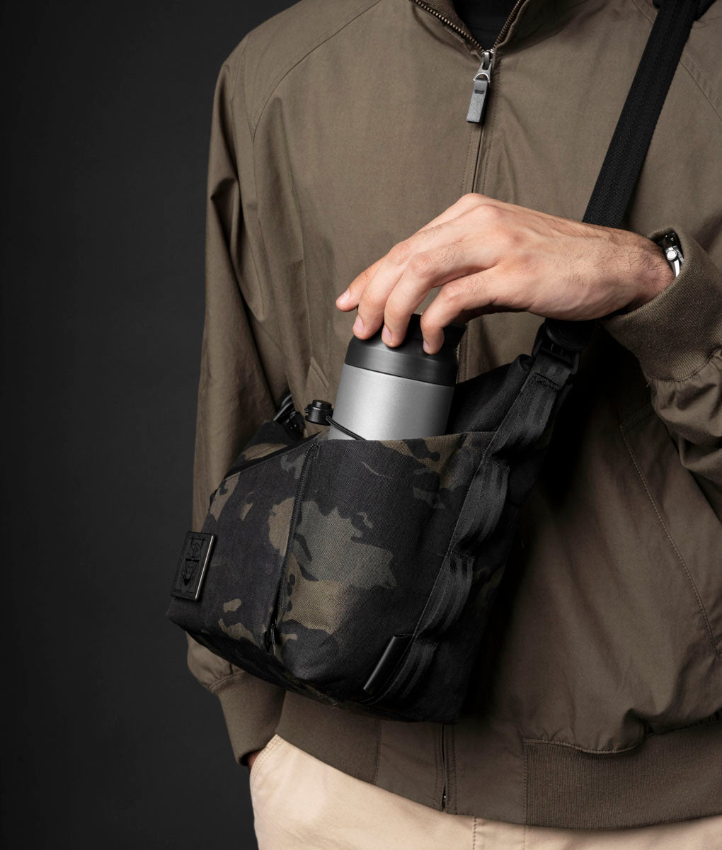 A drink bottle being pushed into the expandable side sleeve of the ClogTwo Edition satchel