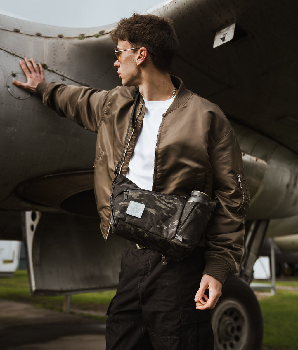 A man wearing the ClogTwo Edition satchel under the wing of a vintage aircraft