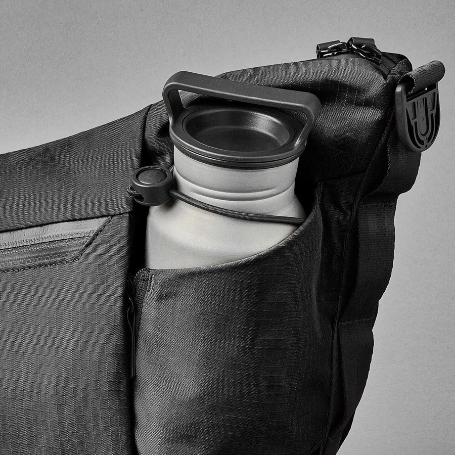 Drink bottle secured in the expandable side sleeve of a black Flow Satchel